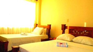 Habitación de hotel con dos camas individuales, cada una con cabecero de madera y ropa blanca. En cada cama, un mesita de noche con lámpara.