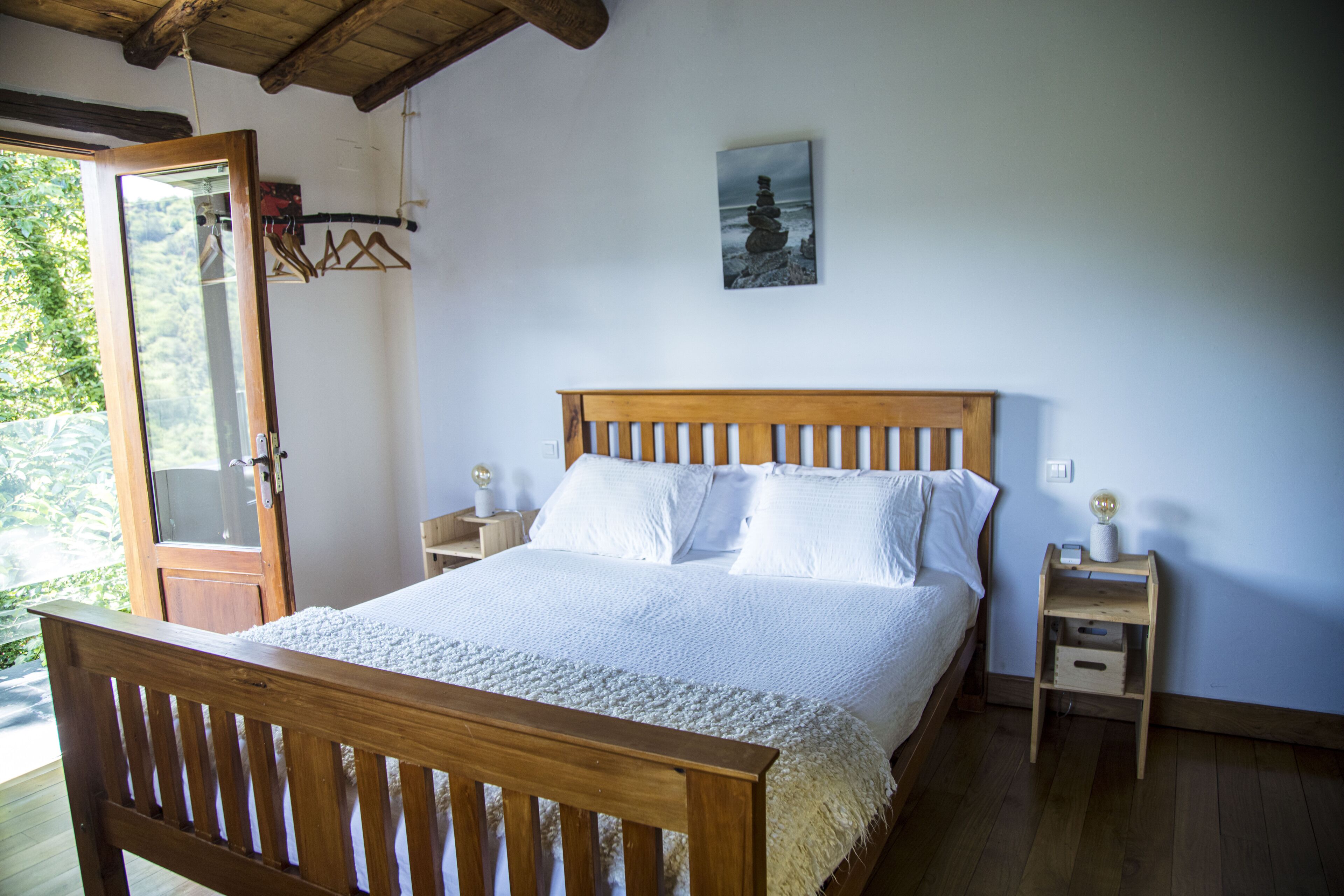 A bedroom with a wooden bed, white bedding, a nightstand with a lamp, and a wall-mounted picture.