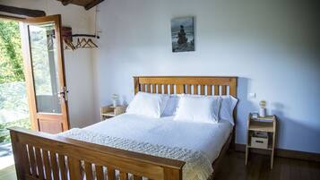 A bedroom with a wooden bed, white bedding, a nightstand with a lamp, and a wall-mounted picture.