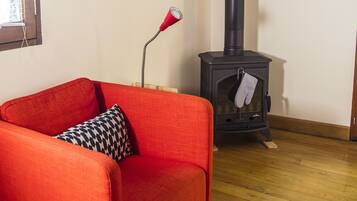 A room with a red sofa, a black and white patterned pillow, a red lamp, a wooden floor, a black chimney, and a blue painting on the wall.