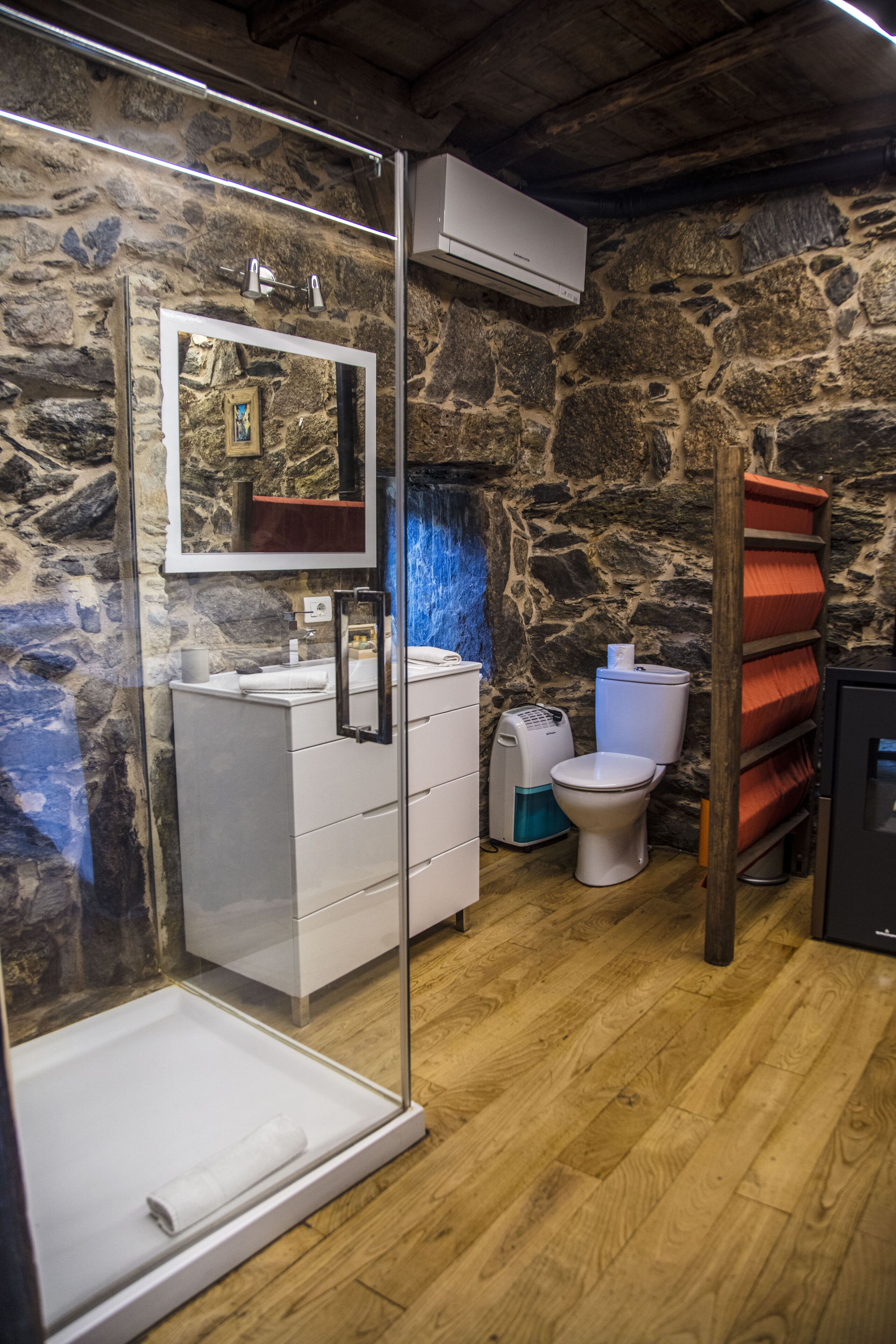 A bathroom with a stone wall, a white sink with a mirror, a toilet, and a shower enclosure.