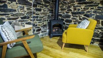 A cozy room with a stone wall, a black wood-burning stove, a yellow armchair, and a green armchair.