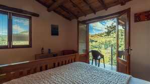 A bedroom with a wooden bed, a view of the outdoors, and a balcony with a chair. - Cabo Do Mundo Casa Rural (Chantada)