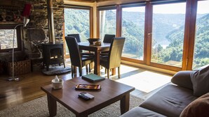 A cozy room with a stone fireplace, wooden dining table, and chairs, overlooking a scenic valley. - Cabo Do Mundo Casa Rural (Chantada)