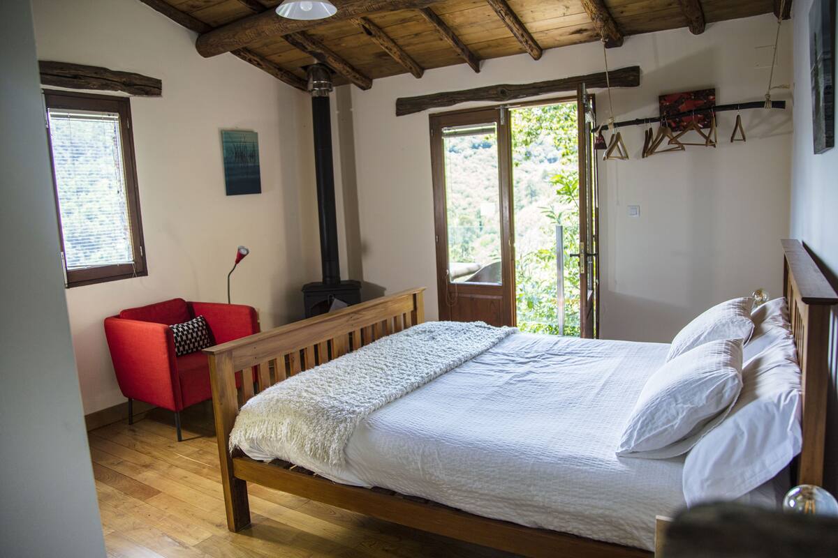 Ein Schlafzimmer mit einem hölzernen Bett, einem roten Sessel und einem großen Fenster.