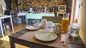 A breakfast table with a plate, glass, and juice pitcher, set against a stone wall and a checkered tablecloth.
