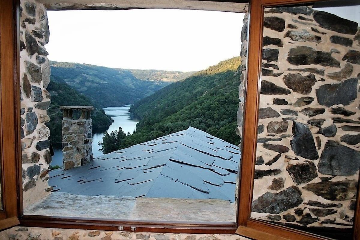 Ein steinrahmiges Fenster mit Blick auf ein Tal, einen Fluss und bewaldete Hügel.