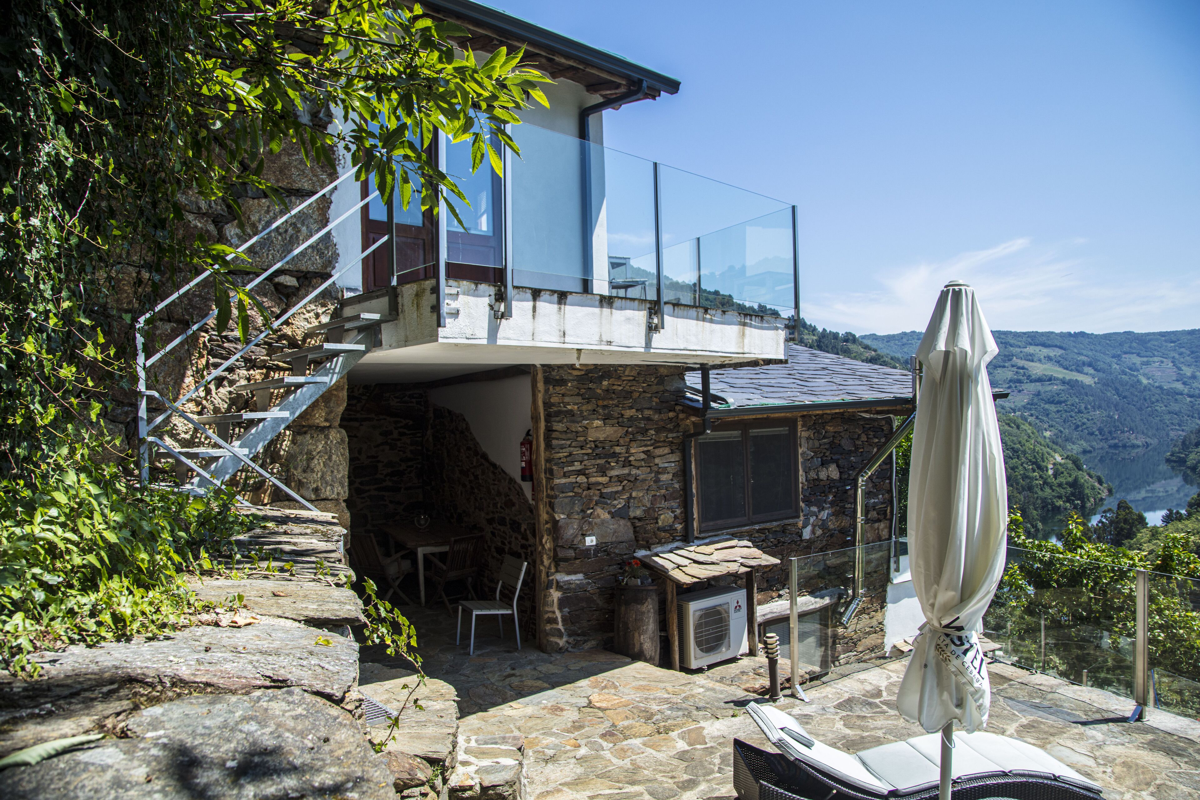 A stone house with a glass balcony overlooking a mountainous landscape.