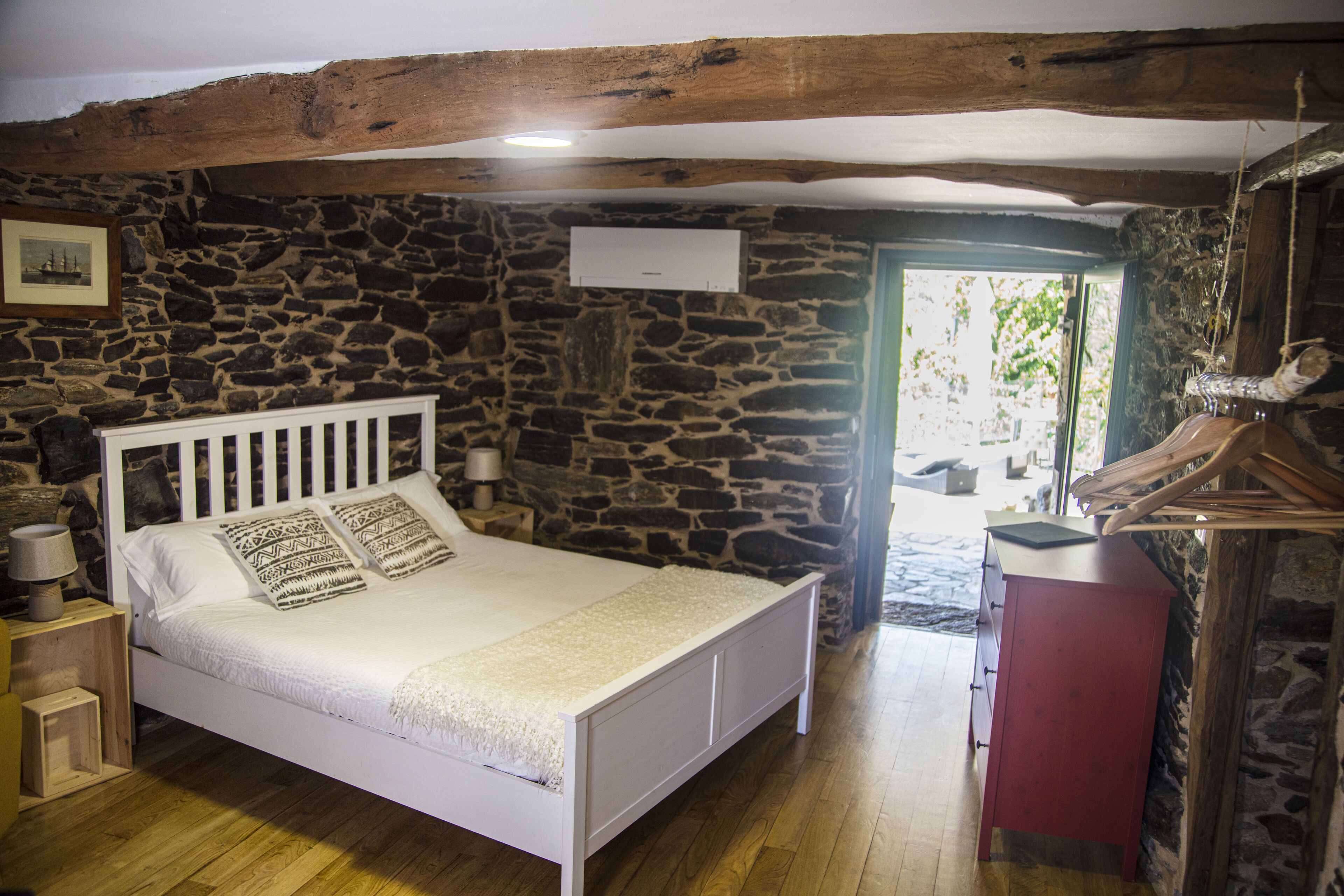 A bedroom with a stone wall, a white bed, a wooden ceiling, and a red cabinet.