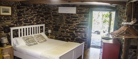 A bedroom with a stone wall, a white bed, a wooden ceiling, and a red cabinet.