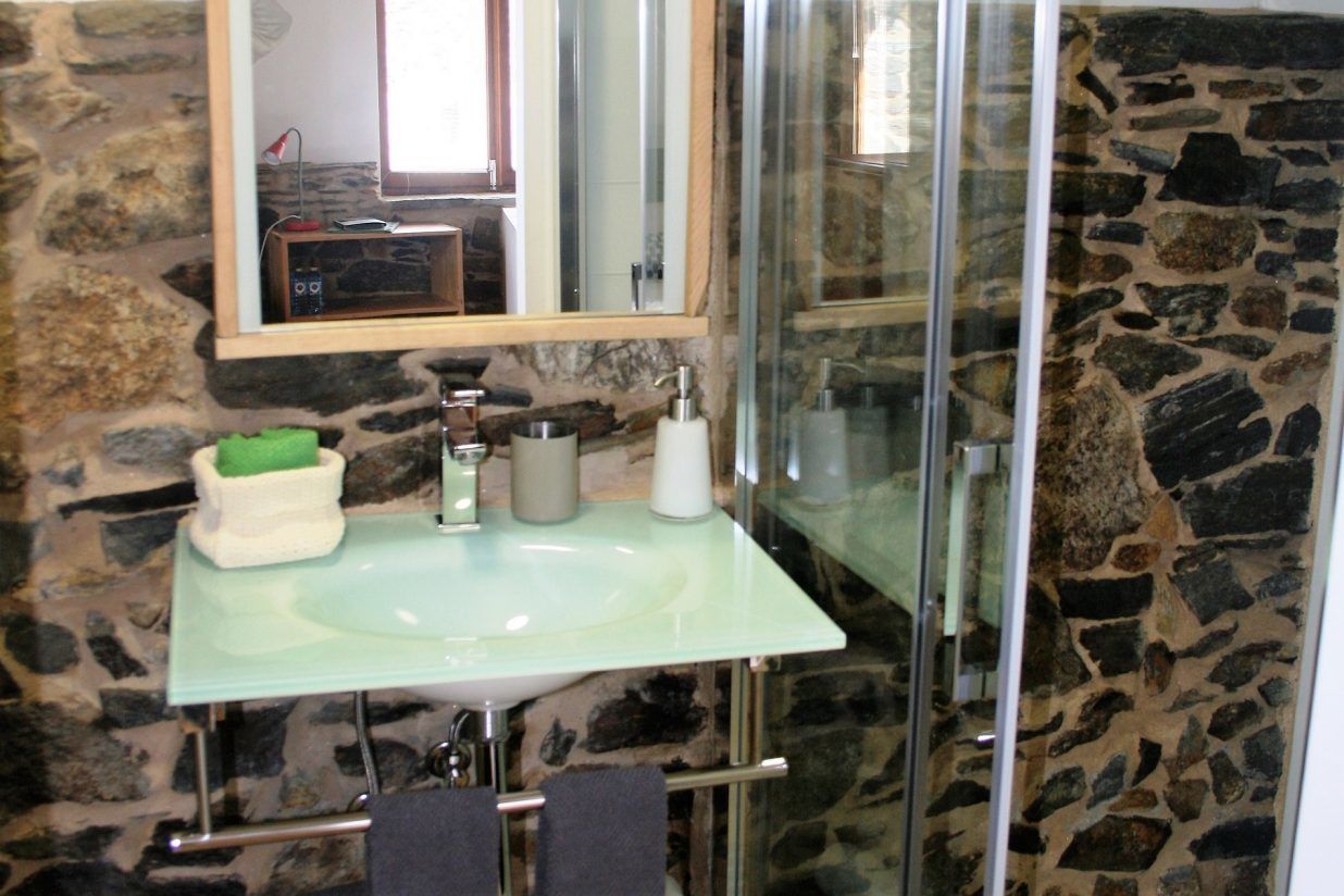 A bathroom with a stone wall, a glass shower enclosure, a sink with a mirror above it, and a towel rack.