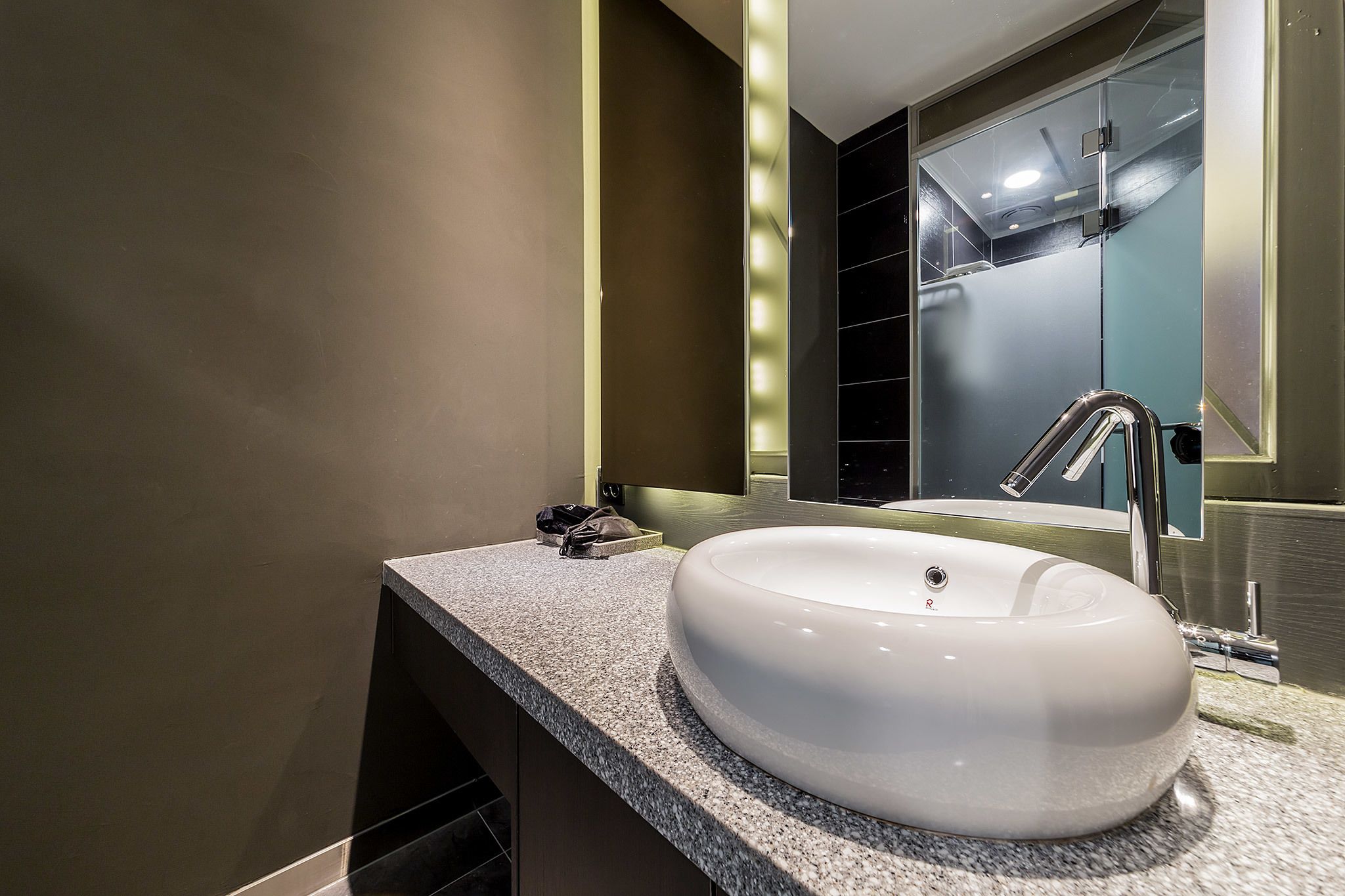 A modern bathroom with a large white sink, a mirror, and a shower area.