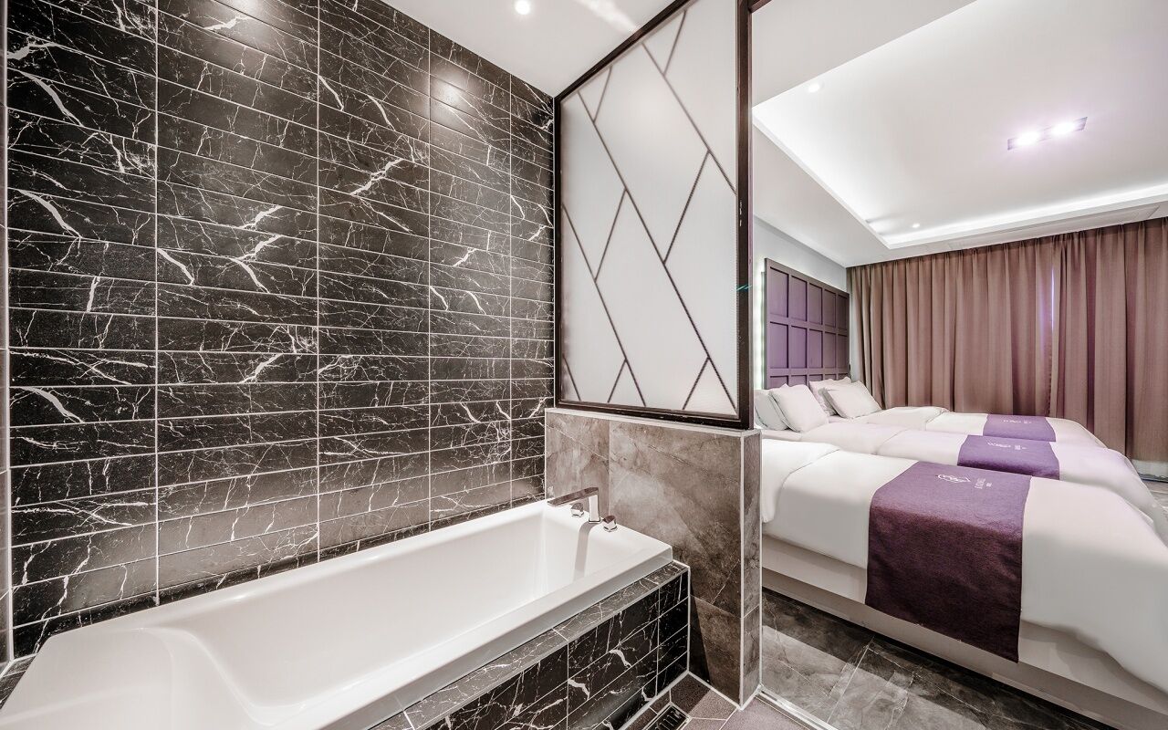 A modern bathroom with a bathtub, marble walls, and a large mirror.