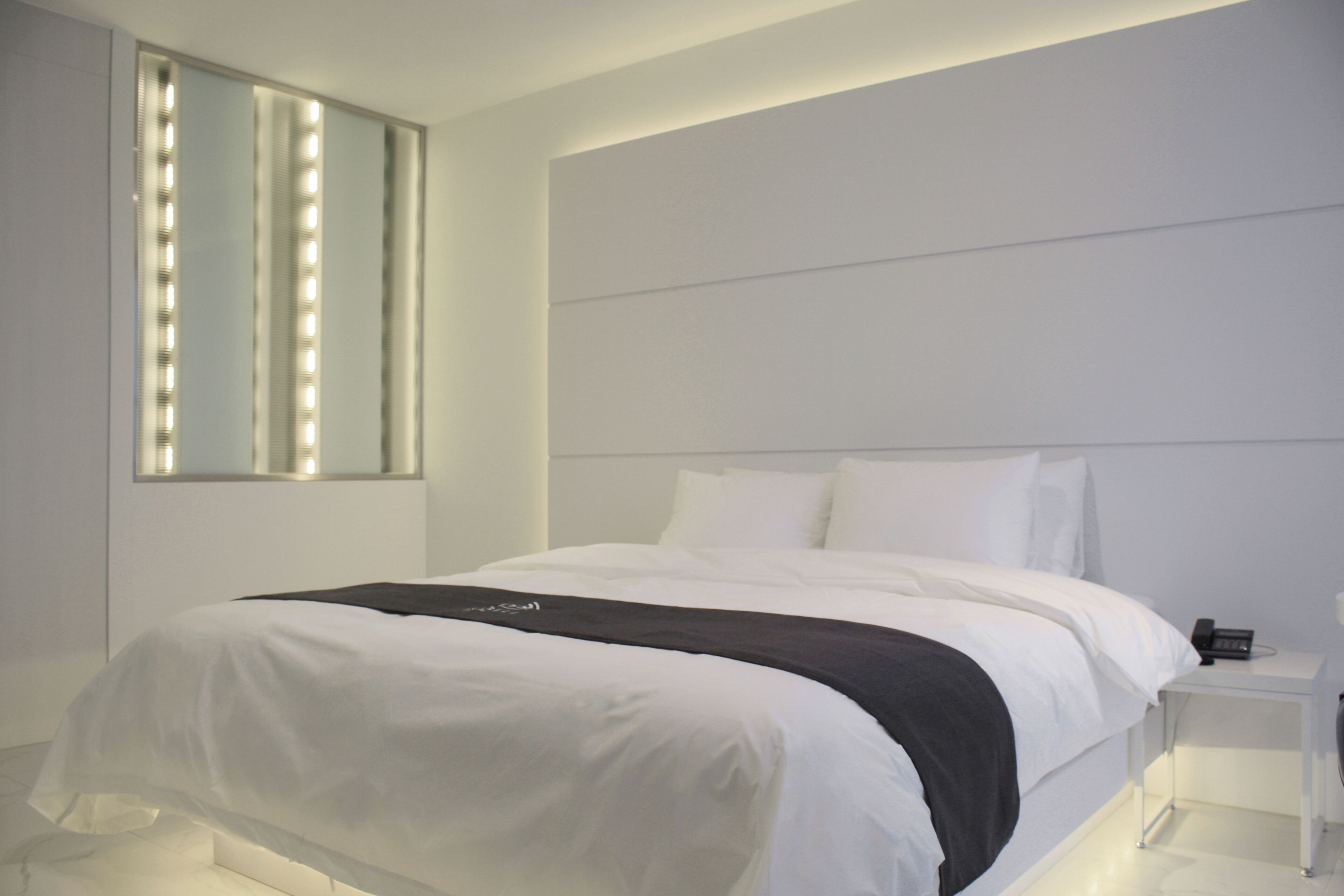 Ett modernt hotellrum med en stor säng, ett sängbord, en spegel och en väggmonterad lampa.