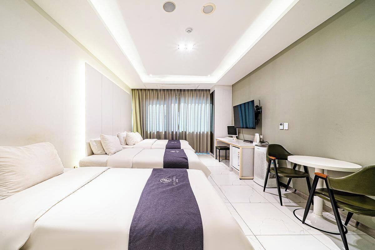 A hotel room with two beds, a desk, a chair, and a TV.