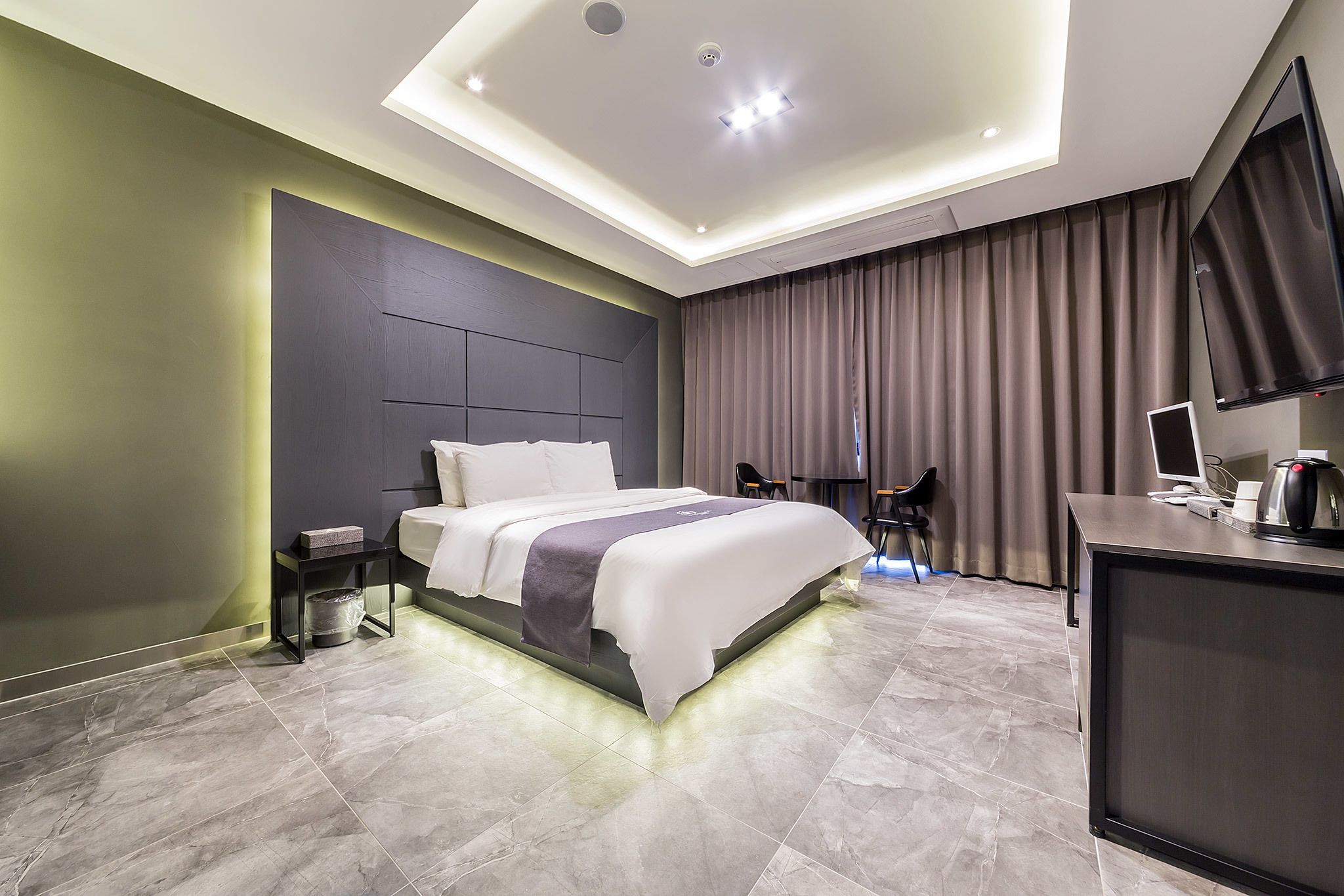 A modern hotel room with a large bed, a desk with a computer, and a TV.