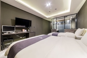Habitación de hotel moderna con una cama grande, un escritorio con computadora, un televisor de pantalla plana y un espejo decorativo.