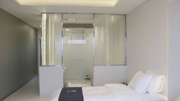 Una habitación de hotel moderna con una cama grande, un vestidor y un box de ducha de vidrio.