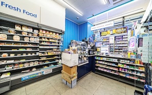 Ein Lebensmittelgeschäft mit Regalen voller verschiedener Lebensmittel, einem Bereich mit der Aufschrift 'Frische Lebensmittel' und einer Theke mit Werbematerialien.