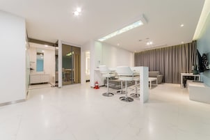 Una habitación de hotel moderna con un diseño espacioso, una zona de comedor con muebles blancos y un amplio ventanal con cortinas.