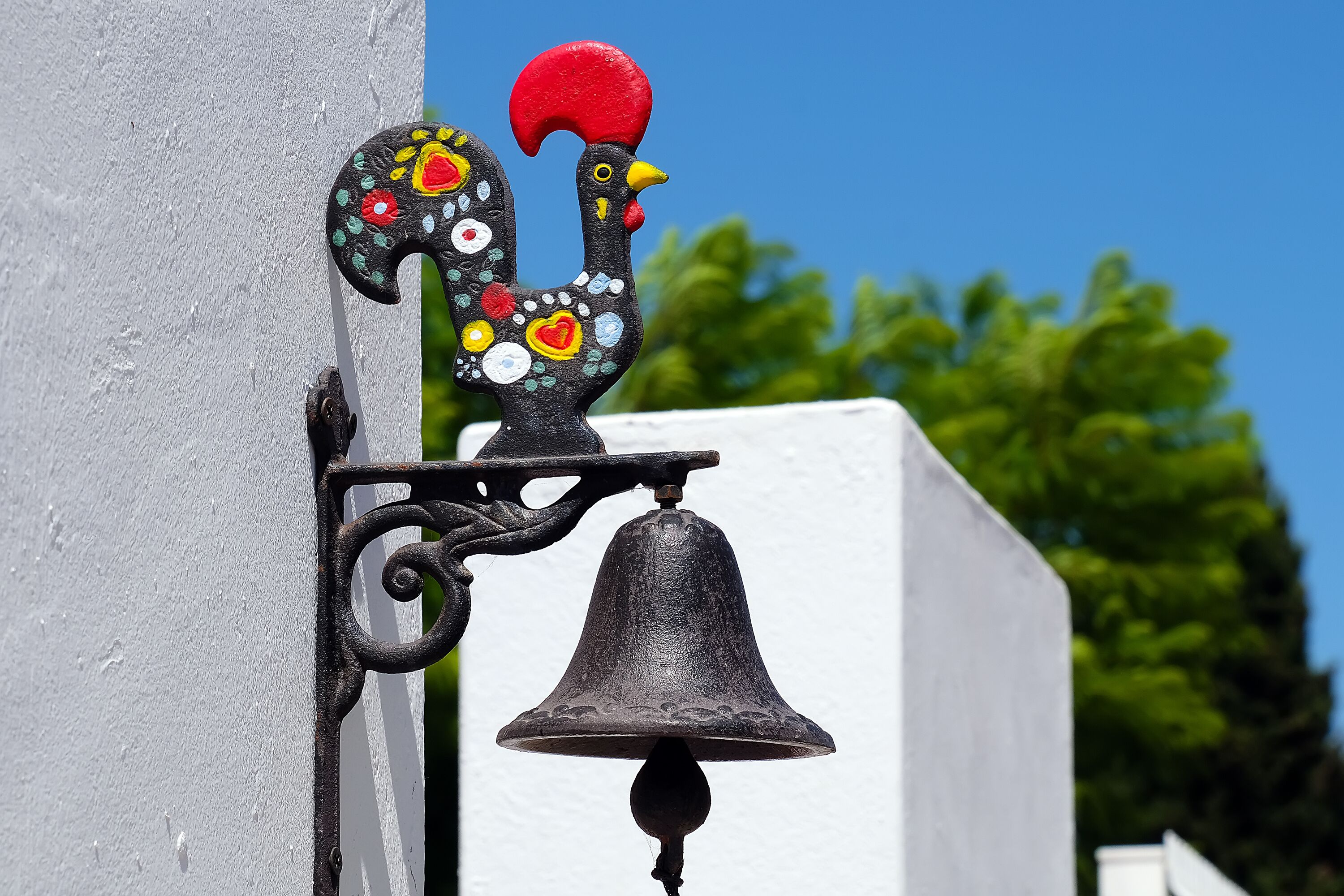 A decorative rooster with a bell attached to a wall.