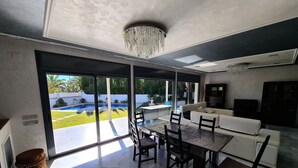 Amplia sala de estar con mesa y sillas de comedor, sofá y televisor. Grandes puertas corredizas de vidrio dan a un patio trasero con piscina.