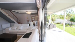 Una sala de estar moderna con un sofá blanco, una mesa de centro oscura y una escalera que lleva a un nivel superior.