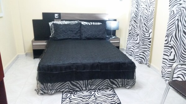 A bedroom with a bed, a nightstand, a lamp, zebra-patterned curtains, and a zebra-patterned rug.