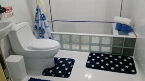 A bathroom with a toilet, sink, and bathtub. There are two star-patterned rugs on the floor.