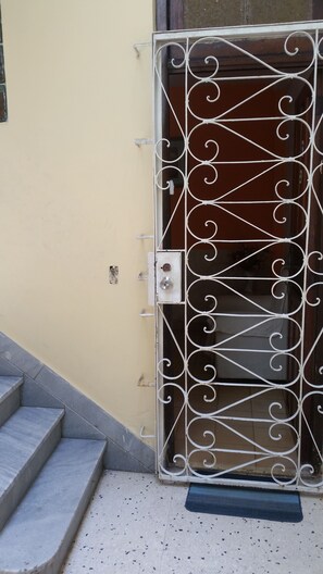 Une porte en métal ornée de motifs complexes, un escalier menant à une porte, et un petit paillasson à l’entrée.