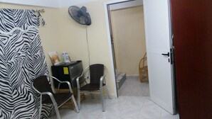 Una stanza con una tenda a motivi zebrati, una scrivania con un computer e documenti, una ventola e una porta che dà su un'altra stanza.