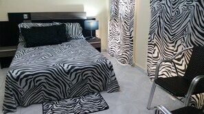 A bedroom with a zebra-striped bedspread, a black pillow, a bedside lamp, and zebra-patterned curtains.