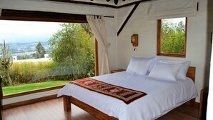Un dormitorio con una cama grande, suelo de madera, vistas a zonas verdes y edificios, y una ventana con cortina.