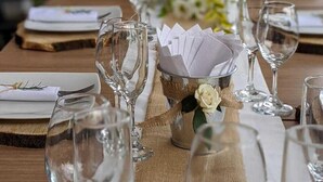 Una mesa puesta para una comida, con cristalería transparente, servilletas dobladas y un centro de mesa con flores.