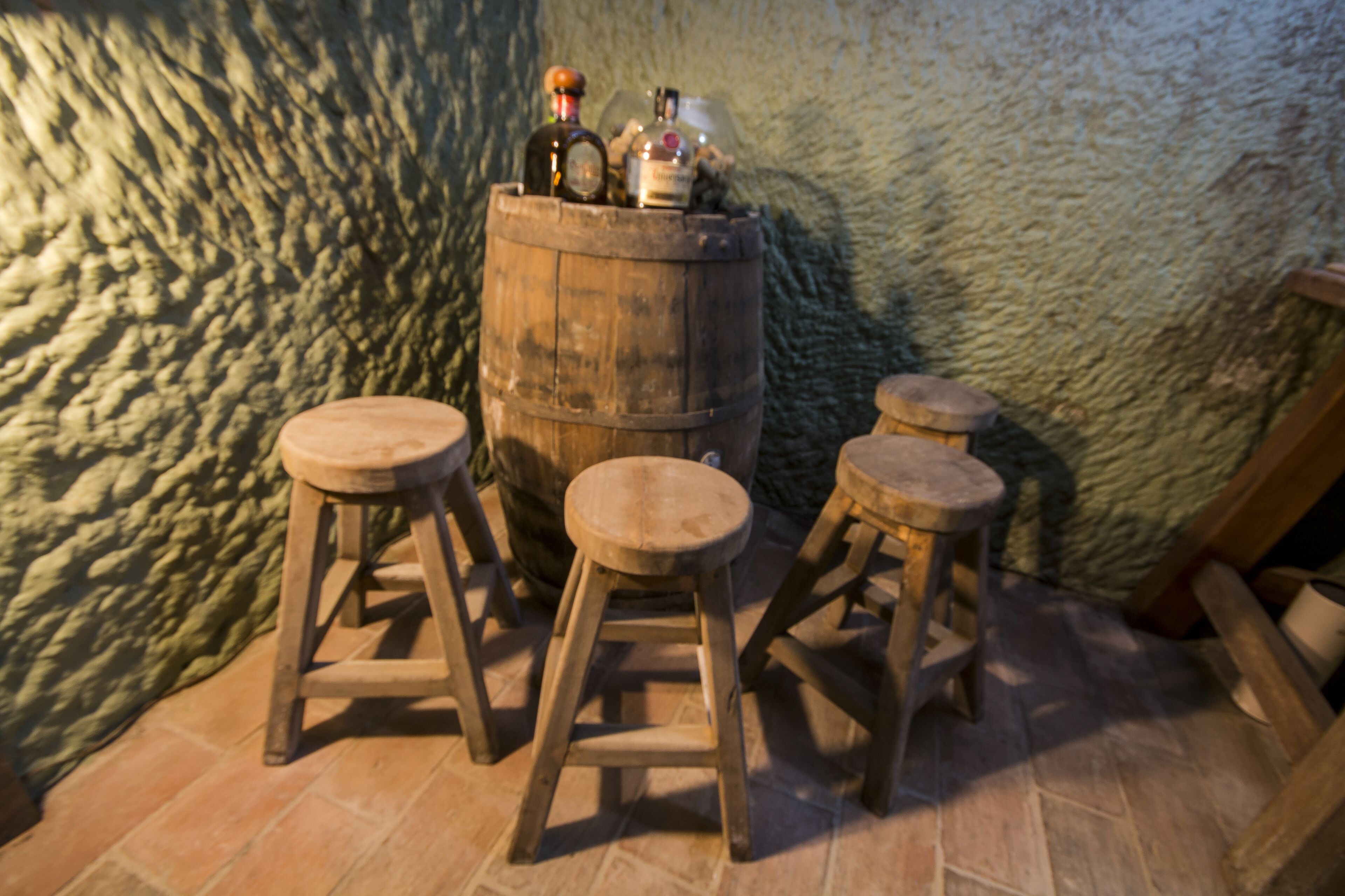 A rustic interior with a wooden barrel, stools, and a textured wall.
