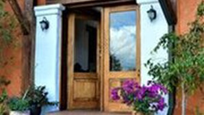 Una puerta de madera con un panel de vidrio, flanqueada por paredes blancas y un zócalo de piedra.