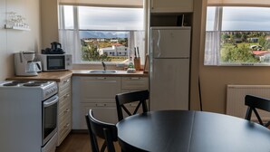A compact kitchen with a dining area, a refrigerator, a microwave, a coffee maker, and a view of the surrounding landscape. - The View Apartments (Fjardabyggd)