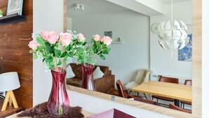 A modern living room with a large mirror reflecting a dining area, a wooden wall, and a red vase with flowers on a wooden stand. - 1209 Bart´s Apartment 9 (Gaschurn)