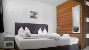 A neatly made bed with white linens and pillows, a wooden headboard, a bedside table with a lamp, and a wall-mounted picture of a deer. - 1209 Bart´s Apartment 9 (Gaschurn)