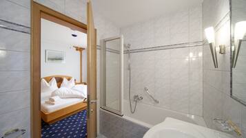Een hotelbadkamer met een douche, een bad en een bed met witte lakens.