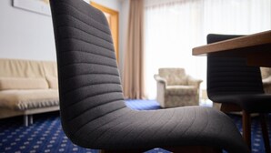 A room with a dark upholstered chair, a wooden table, a beige sofa, and a patterned carpet. - 1105 Veilchen (Gaschurn)