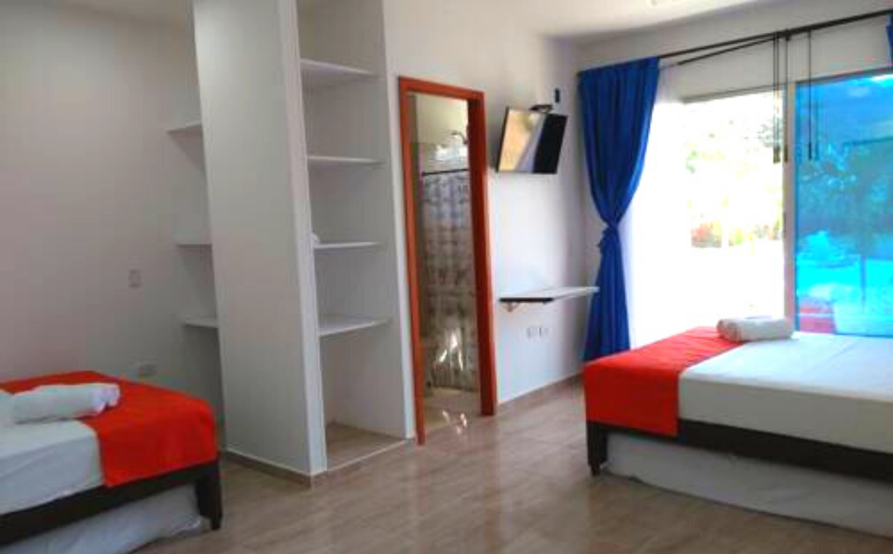 Habitación de hotel con dos camas, un armario, un espejo y una ventana con cortinas.