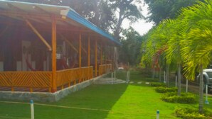 A covered outdoor area with a wooden structure, a grassy lawn, and palm trees. - Cabañas Vacacionales En Palomino Guajira (Dibulla)