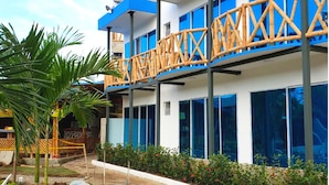 A modern building with a blue and white exterior, large windows, and a bamboo railing on the upper level. - Cabañas Vacacionales En Palomino Guajira (Dibulla)
