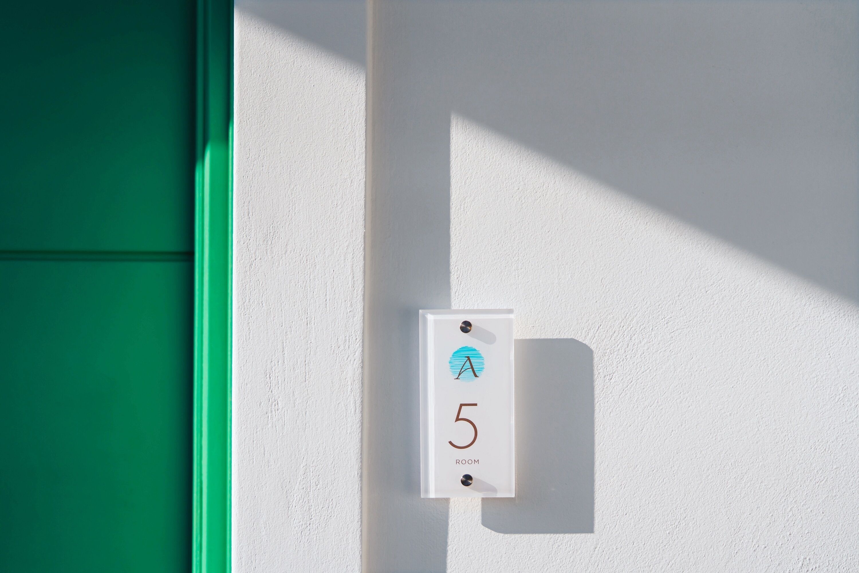 A white wall-mounted sign with a blue circle, the number 5, and the word "ROOM" indicating a room number.