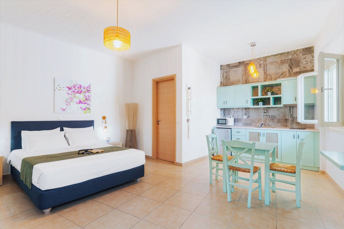 A bedroom with a bed, a desk, and a kitchenette.