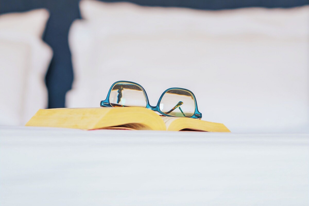 Un lit avec des oreillers blancs et un livre sur lequel reposent des lunettes.