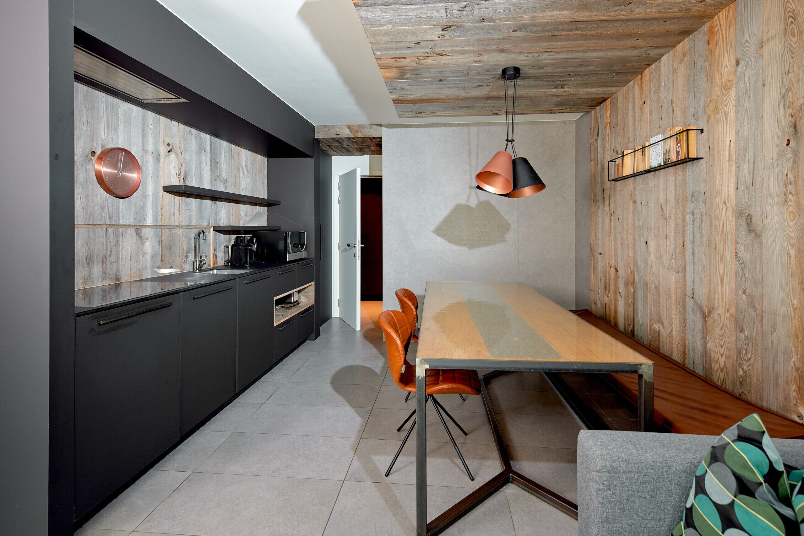 Eine moderne Küche mit dunklen Schränken, einer Holzwand und einem Essbereich mit Tisch und Stühlen.