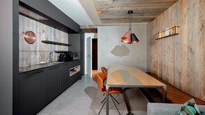 A modern kitchen with dark cabinetry, a wooden wall, and a dining area with a table and chairs.