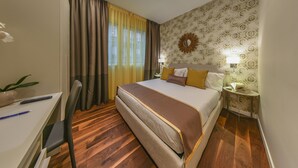 Habitación de hotel con cama, mesita de noche, lámpara y escritorio con silla.